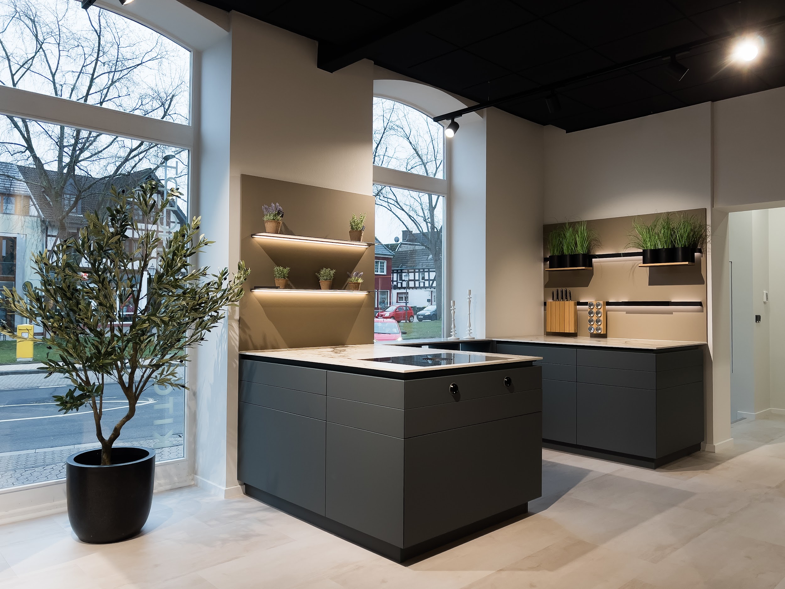 Anthrazitfarbene Kücheninsel mit Arbeitsplatte in Marmoroptik vor den Rundbogenfenstern des Studios Rheinbach