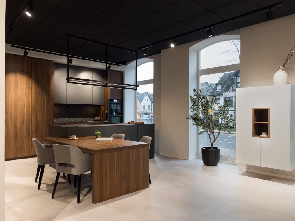 Offene Wohnküche mit dunkler Insel und integriertem Esstisch aus Massivholz.