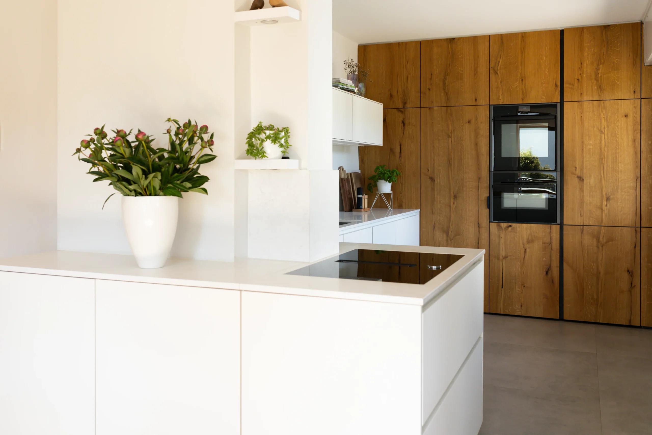 Moderne Designküche in Alfter mit weißer Kochinsel, Massivholzfronten und integrierten Neff-Einbaugeräten