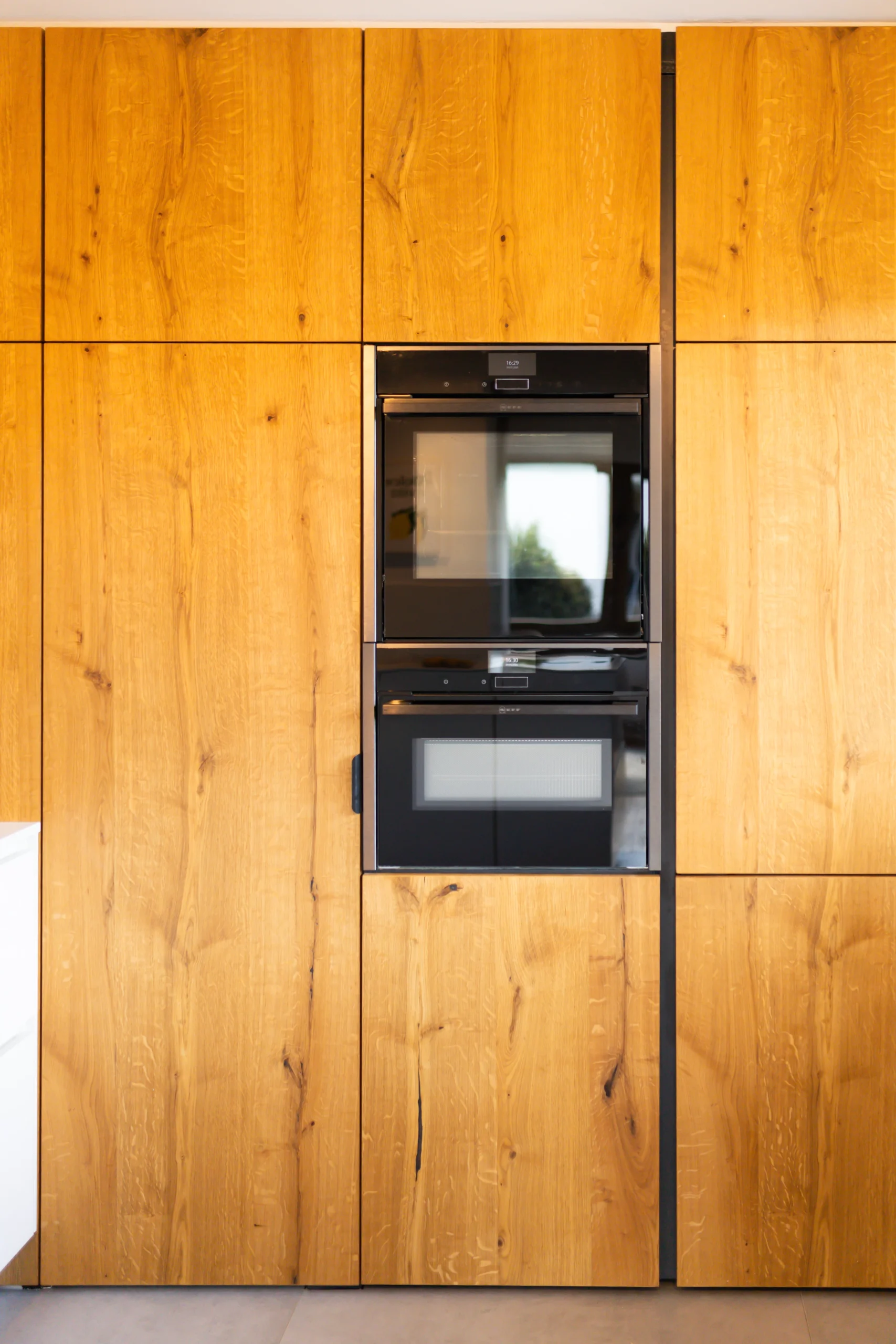 Detailaufnahme Massivholzfront mit durchgehender Maserung und integrierten Neff-Einbaubacköfen in schwarzem Design