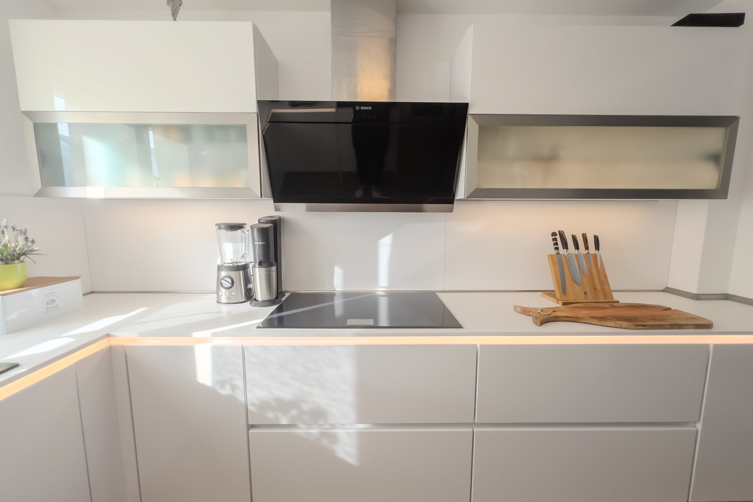 Breites Induktionskochfeld und schräge BOSCH Dunstabzugshaube aus schwarzem Glas und Edelstahl zwischen Oberschränken