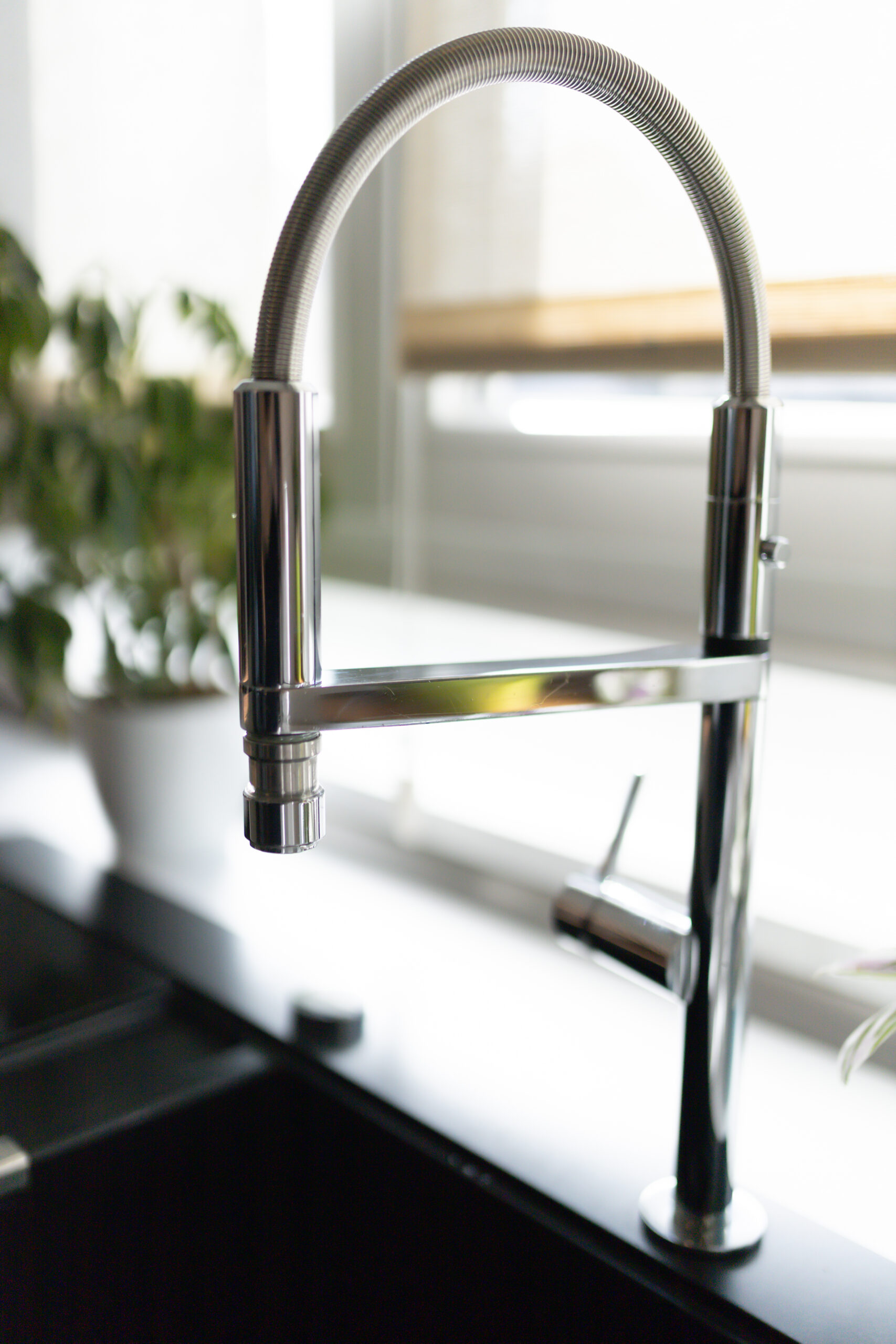 Detailaufnahme einer modernen, glänzenden Chrom-Spültischarmatur mit flexiblem Ausziehschlauch vor dem Küchenfenster