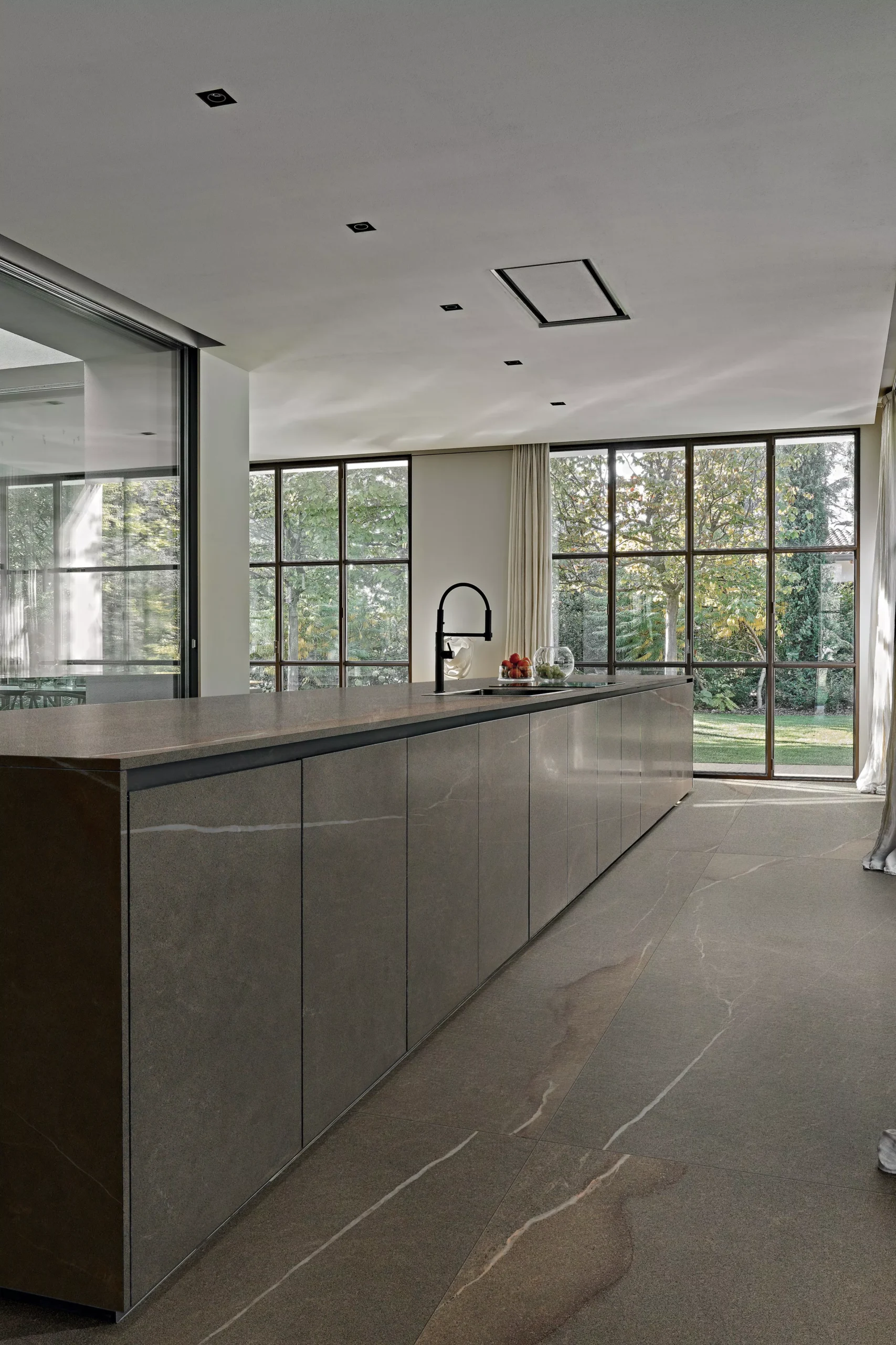 Lange Küchenzeile mit Arbeitsplatte und Fronten in grau-brauner Steinoptik, schwarze Armatur und große Fensterfront