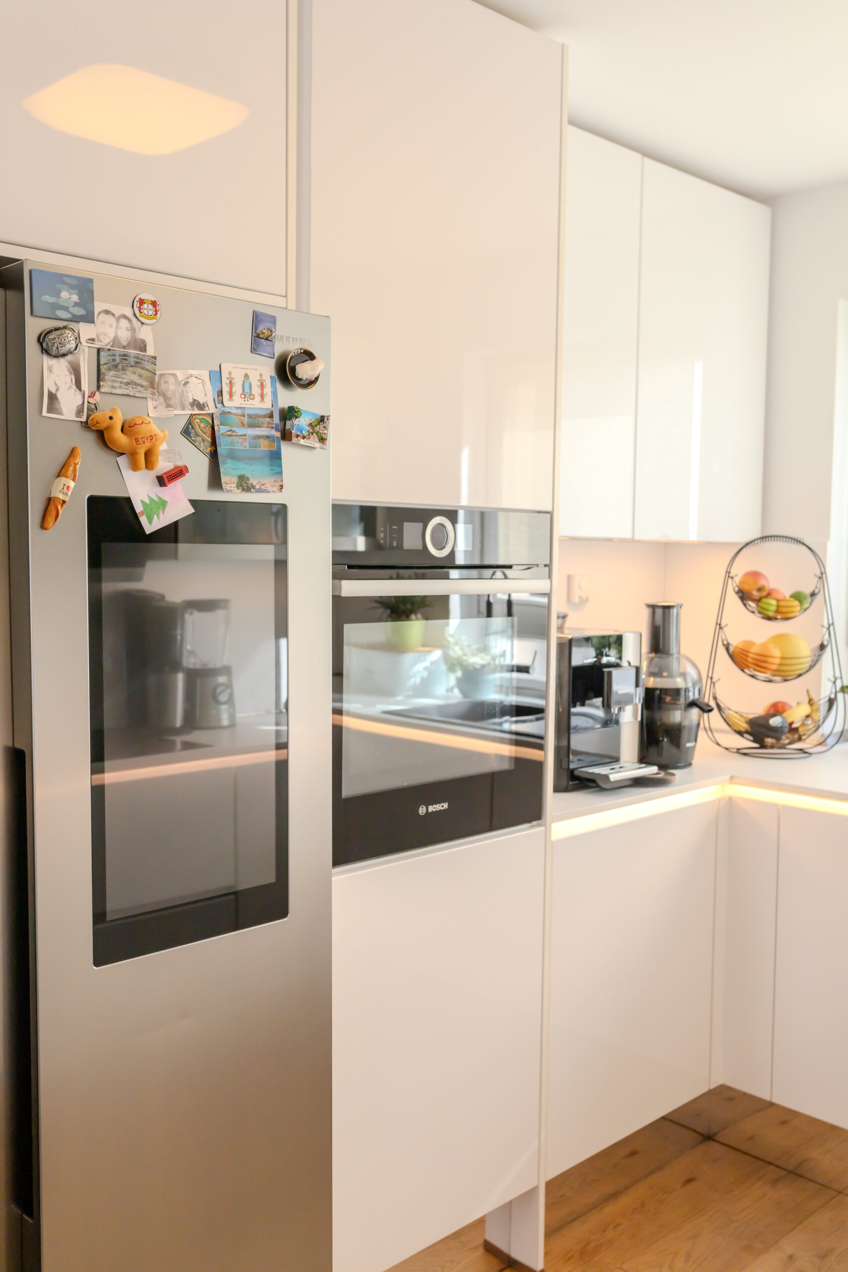 In die weiße Hochschrankwand ergonomisch integrierter BOSCH Backofen neben einem Side-by-Side-Kühlschrank mit Display.