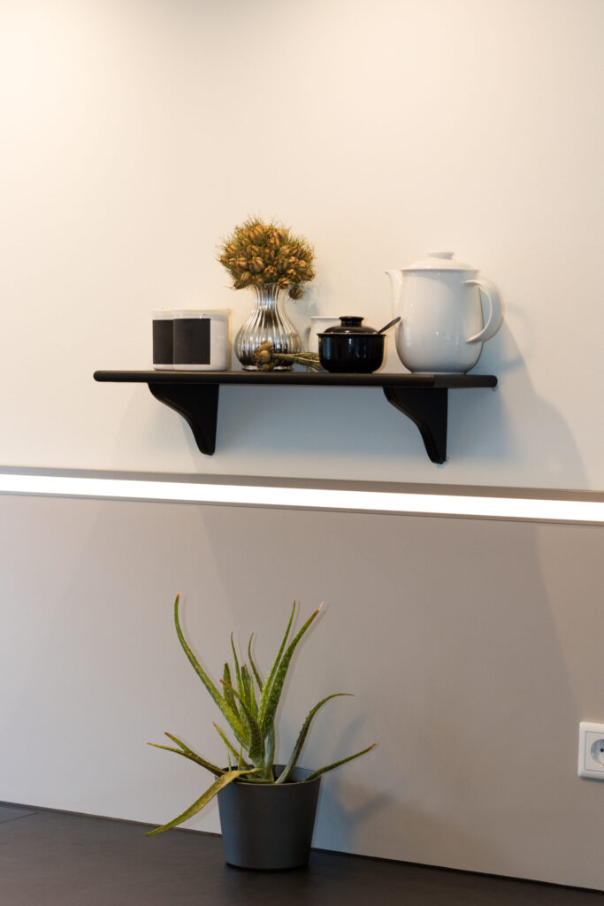 Detailaufnahme eines schwarzen Wandregals über einer beleuchteten Küchen-Nischenrückwand.