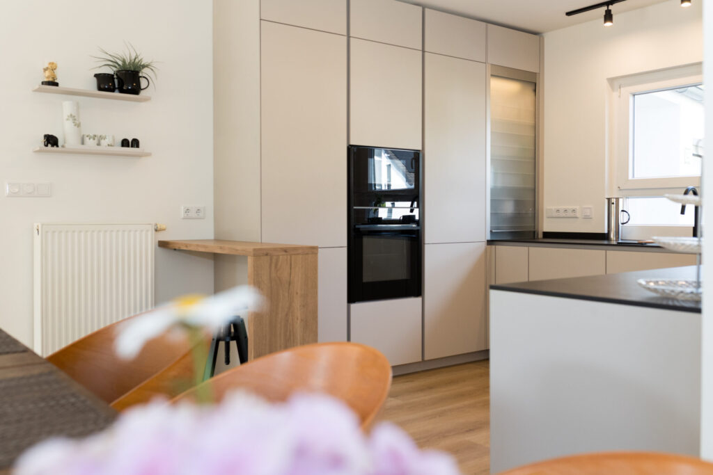 Weitwinkel-Blick über den Esstisch mit Holzstühlen auf die grifflose Küche samt Bartresen und Rollladenschrank.