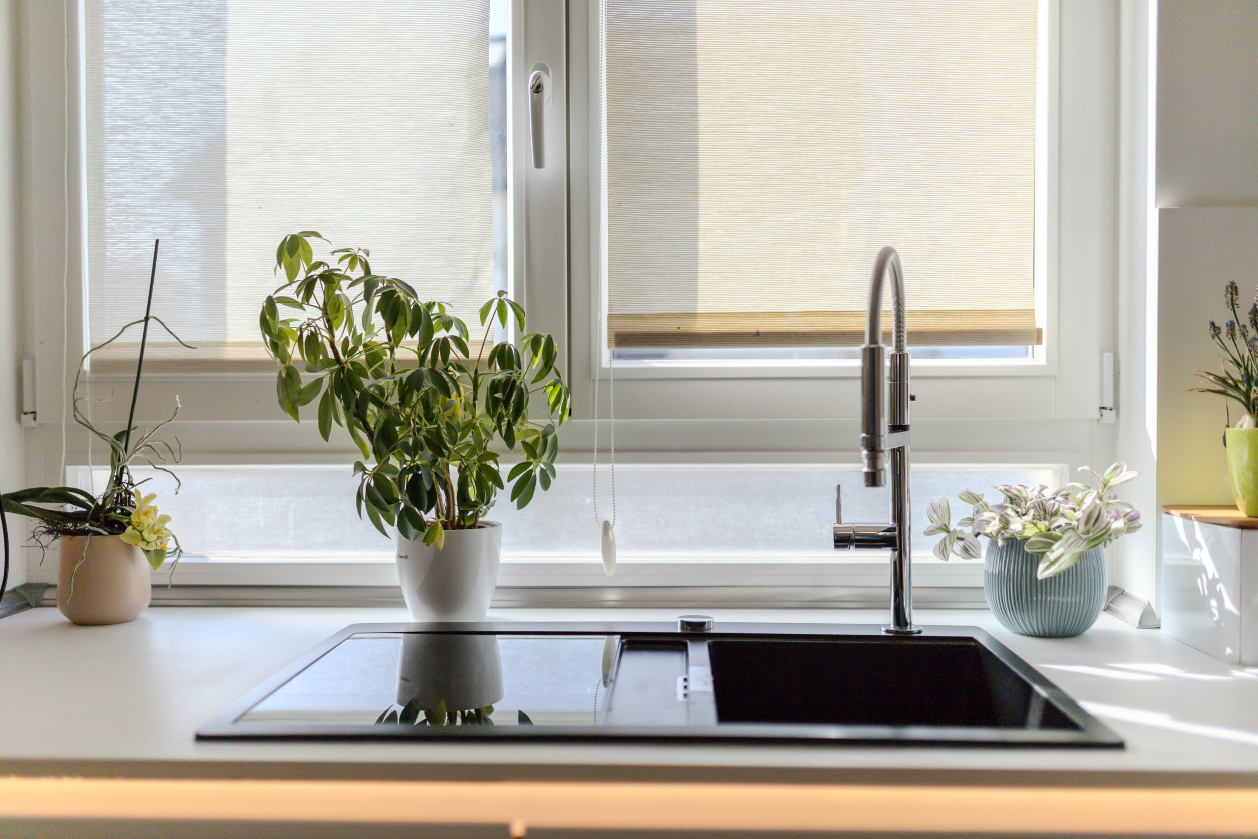 Schwarzes Spülbecken flächenbündig integriert vor dem Fenster mit Design-Armatur und dezent beleuchteter Kante.